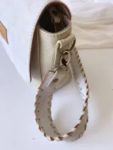 Bandolera color crudo con solapa de gamuza y cuerpo de cuero sintético texturizado. Tiene correa corta de cuero con tientos y forro de tela con bolsillo interno.