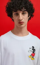 Remera oversize de algodón premium color blanco, con cuello redondo y manga corta. Presenta un pequeño estampado del personaje Mickey Mouse en el lado izquierdo del pecho.