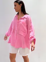 Camisa oversize rosada de lino, con cuello clásico, cierre frontal con botones, dos bolsillos de parche en el pecho y mangas largas con puños abotonados.