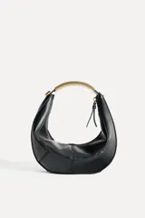Bolso negro de formato ovalado con asa metálica dorada. Tiene detalle de pespunte en contraste en el cuerpo, bolsillo interior con cremallera y cierre mediante cremallera y tirador.