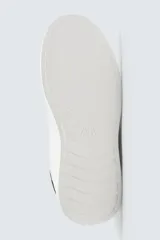 Zapatillas blancas de cuero sintético, con cordones y detalle de pieza a contraste en color negro en la parte posterior. Suela de goma blanca con volumen de diseño irregular.