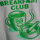 Buzo gris con cuello redondo y puños y cintura acanalados. Estampado pequeño en el pecho con la leyenda "420 Breakfast Club" en color verde.