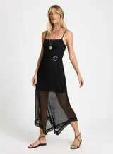 Vestido midi negro de lurex con breteles finos, corte ajustado y falda asimétrica con volados. Incluye cinturón de soga con hebilla dorada.