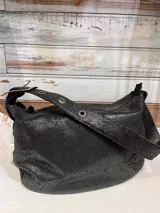 Bolso de hombro tipo hobo confeccionado en gamuza color marrón con textura de cuadrícula. Posee una correa ancha ajustable con hebilla metálica y ojalillos, cierre superior y compartimentos internos.
