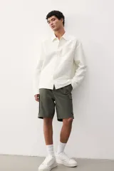 Short cargo color verde militar, de corte regular, con cintura elástica ajustable con cordón, bolsillos laterales, bolsillos cargo con solapa y cierre autoadherente en las piernas y bolsillos traseros con solapa y cierre autoadherente.