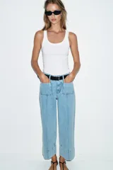 Jeans de tiro alto con corte wide leg cropped, confeccionados en denim de lavado claro. Presentan costuras marcadas en el frente, bolsillos de plastrón delanteros y cierre frontal con cremallera y botón.