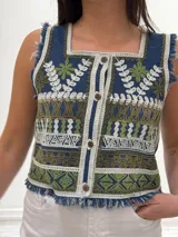 Chaleco corto de denim azul con bordado artesanal en tonos naranja, blanco y marrón. Tiene escote cuadrado, cierre de botones y terminaciones desflecadas.