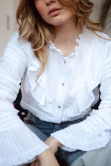 Camisa blanca de algodón con volados en el pecho y cuello, botones nacarados y mangas largas con puños elásticos.