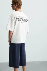 Camiseta blanca de corte holgado, cuello redondo y manga corta. Presenta estampados combinados en negro en la parte delantera y trasera.