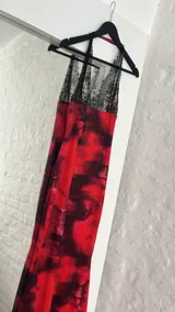 Vestido largo de tirantes finos con encaje negro en el escote y estampado abstracto en tonos rojos y negros.