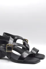 Sandalias negras con tiras cruzadas, hebilla dorada y taco ancho.