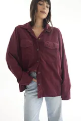 Camisa oversize color borgoña de pana con cuello camisero, cierre frontal con botones, dos bolsillos con solapa en el pecho y mangas largas con puños abotonados.