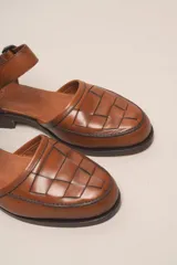 Zapato marrón de cuero con correa al tobillo y hebilla negra. Diseño trenzado en la parte delantera.