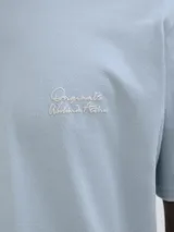 Camiseta celeste de manga corta y cuello redondo con estampado en el frente que dice 'Studio Originals Edition'.
