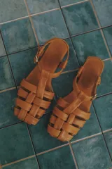 Sandalias franciscanas color cuero, con tiras anchas de cuero entrelazadas en el empeine, tira trasera con hebilla y suela plana de cuero.