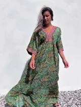 Vestido túnica largo con estampado paisley en tonos verdes, amarillos y rojos. Presenta escote en V con bordado decorativo y mangas 3/4 amplias.