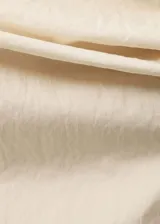 Blusa color crema sin mangas, con cuello asimétrico drapeado y corte recto.