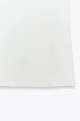 Top blanco de tejido elástico con escote cuadrado y tirantes con lazos decorativos. Tiene forro interior y cierre lateral con cremallera oculta.