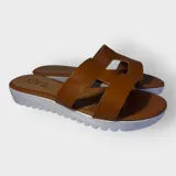 Sandalias tipo slide de color tostado, con tiras cruzadas y suela blanca texturada.