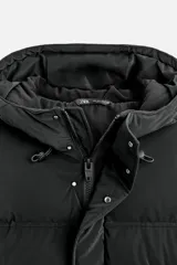 Cazadora acolchada negra de tejido técnico, cuello alto con capucha ajustable, manga larga con puño interior elástico, bolsillos laterales y bolsillo interior. Cierre frontal con cremallera oculta y botones a presión.