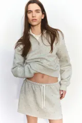 Minifalda gris melange de tejido suave con efecto neopreno y strass brillante. Tiene corte holgado, cintura elastizada con cordón ajustable y no está forrada.