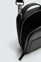 Bandolera negra con textura grabada, forma rectangular y cierre de cremallera. Tiene un bolsillo interior plano y otro frontal plano. Incluye asa de hombro ajustable y extraíble.