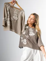 Sweater tejido en hilo color beige, con apliques bordados de flores blancas y detalles de perlas.