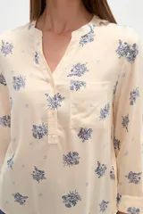Blusa de manga tres cuartos color crema con estampado floral en azul. Presenta cuello mao con abertura en V y un bolsillo de parche en el pecho.