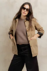 Campera color beige con cuello de corderito negro, cierre con botones, bolsillos laterales y puños con detalle de cuero sintético negro.