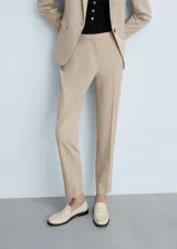 Pantalón de vestir color beige, de corte recto, con bolsillos laterales y traseros. Se ajusta a la cintura con cinturón de cuero marrón.