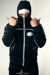 Campera negra de algodón impermeable con doble capucha, una de ellas tipo pasamontañas. Presenta viras y logos reflectivos, y cierres de metal. La parte trasera tiene un estampado de estrella con tachas.