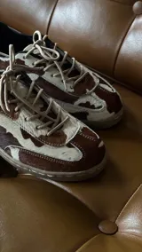 Sneakers de cuero con estampado de vaca en tonos marrón y blanco, con cordones beige y suela de goma color caramelo.