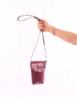 Cartera porta celular de cuero color bordó, con correa larga y solapa con tachas plateadas.