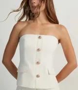 Blusa estilo corset color blanco, con escote recto, sin mangas, abotonado frontal y solapas aplicadas.
