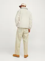 Campera de teddy color blanco hueso, de manga larga y cuello alto. Tiene cierre con cremallera, bolsillos frontales y un bolsillo gris en el pecho con cierre.