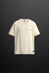 Camiseta color crudo de corte relaxed fit confeccionada en tejido técnico ligero de tacto suave, cuello redondo y manga corta. Tiene un texto estampado en el delantero y detalle de logo estampado en el bajo.