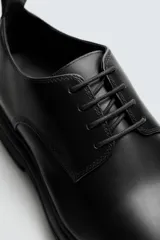 Zapato de vestir estilo derby, color negro, con capellada de cuero, horma redonda y suela de goma con volumen.