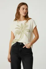 Blusa de viscosa color crudo con estampado de palmera verde, corte holgado, cuello redondo y mangas cortas.