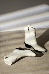 Bota corta de cuero sintético color blanco, estilo texana con bordados decorativos y taco cubano negro.