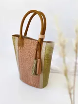 Bolso matero de cuero color nude con textura croco y laterales en color pistacho. Tiene manijas cortas de cuero color suela y un dije de cuero con flecos.
