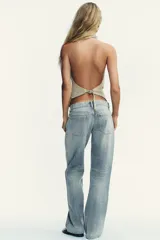 Pantalón de jean celeste claro, de tiro bajo, corte wide leg y largo hasta el tobillo. Tiene cinco bolsillos, cierre frontal con cremallera y botón metálico.