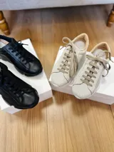 Zapatillas deportivas urbanas de cuero negro y beige con cordones y suela gruesa.