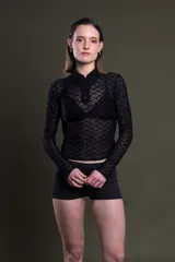 Polo de manga larga color negro, confeccionada en encaje con diseño geométrico. Tiene cuello polo con cierre de cremallera y es traslúcida.