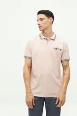 Chomba de piqué color rosa claro, de corte clásico, con cuello y mangas con ribete a rayas en blanco, gris y negro. Tiene tapeta de dos botones y logo bordado en el pecho.