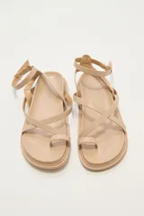 Sandalias marrones con tiras cruzadas y tobillera con hebilla dorada.