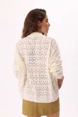 Cárdigan tejido calado color crudo con cierre frontal, cuello alto y mangas largas.