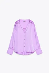 Camisa lila de satén con cuello solapa, escote en pico y manga larga. Tiene detalle de lazada en la espalda, bajo con aberturas laterales y cierre frontal con botones.