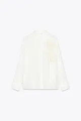 Camisa blanca de manga larga con cuello solapa y bordado de flor en el frente.