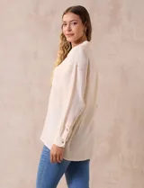 Camisa blanca de algodón con textura arrugada, cuello con solapa, abertura central con botones y bolsillo aplicado en el pecho. Mangas largas con largo regulable mediante presilla y botón.