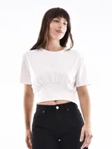 Remera corta color blanco hueso, con cuello redondo y frunce elástico en la cintura.